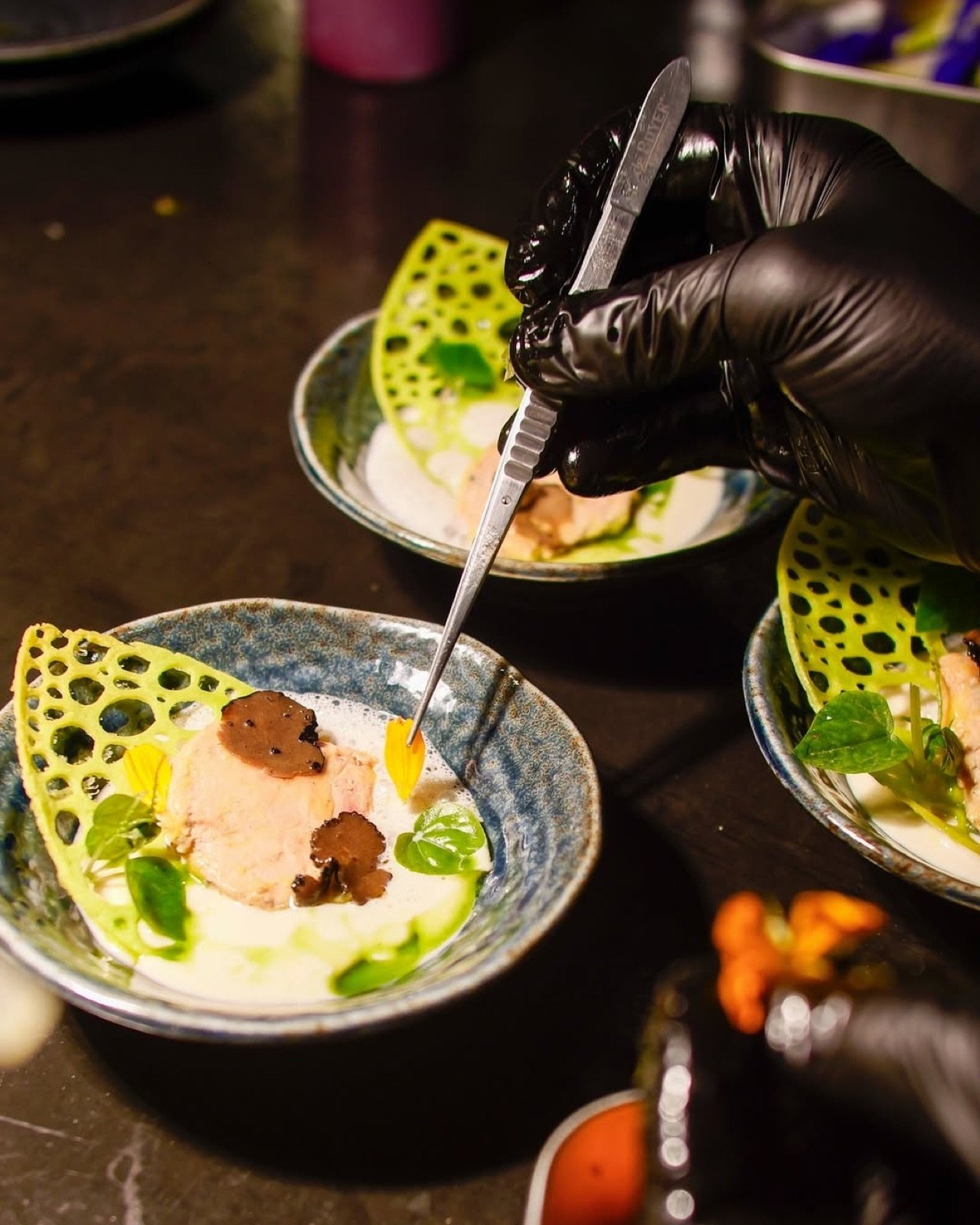 Cuisinier en gants noirs dressant une assiette à la pince